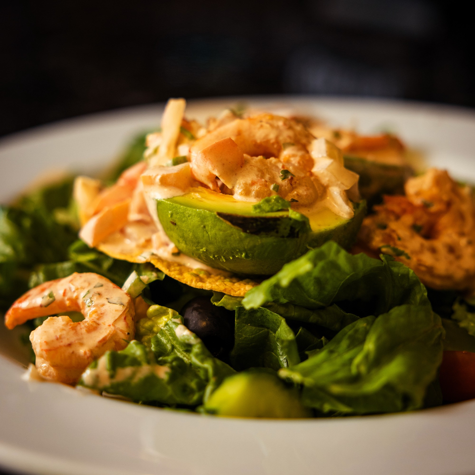 Shrimp and avocado salad with lettuce, tortilla chips, and creamy dressing on a white plate.