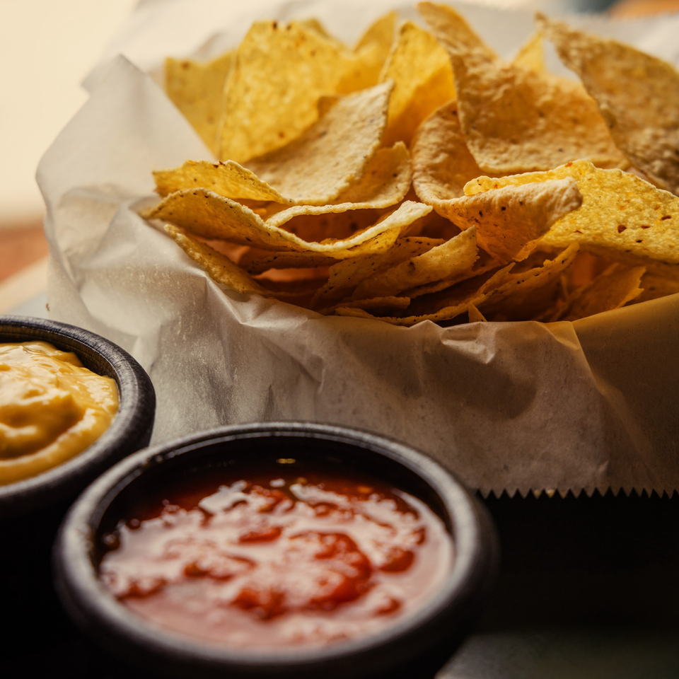 A basket of La Casa del Sol's tortilla chips with small bowls of salsa and queso.