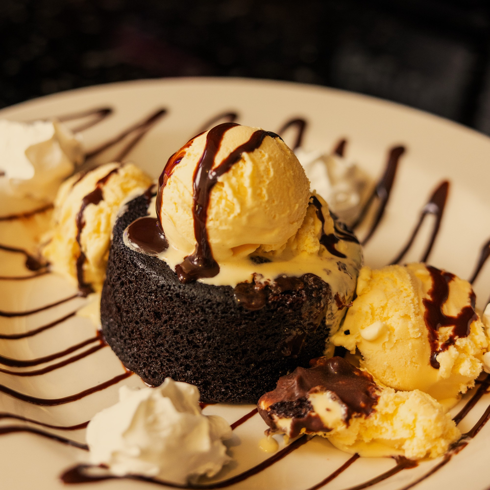 Warm chocolate lava cake with vanilla ice cream, chocolate syrup, and whipped cream on a white plate.