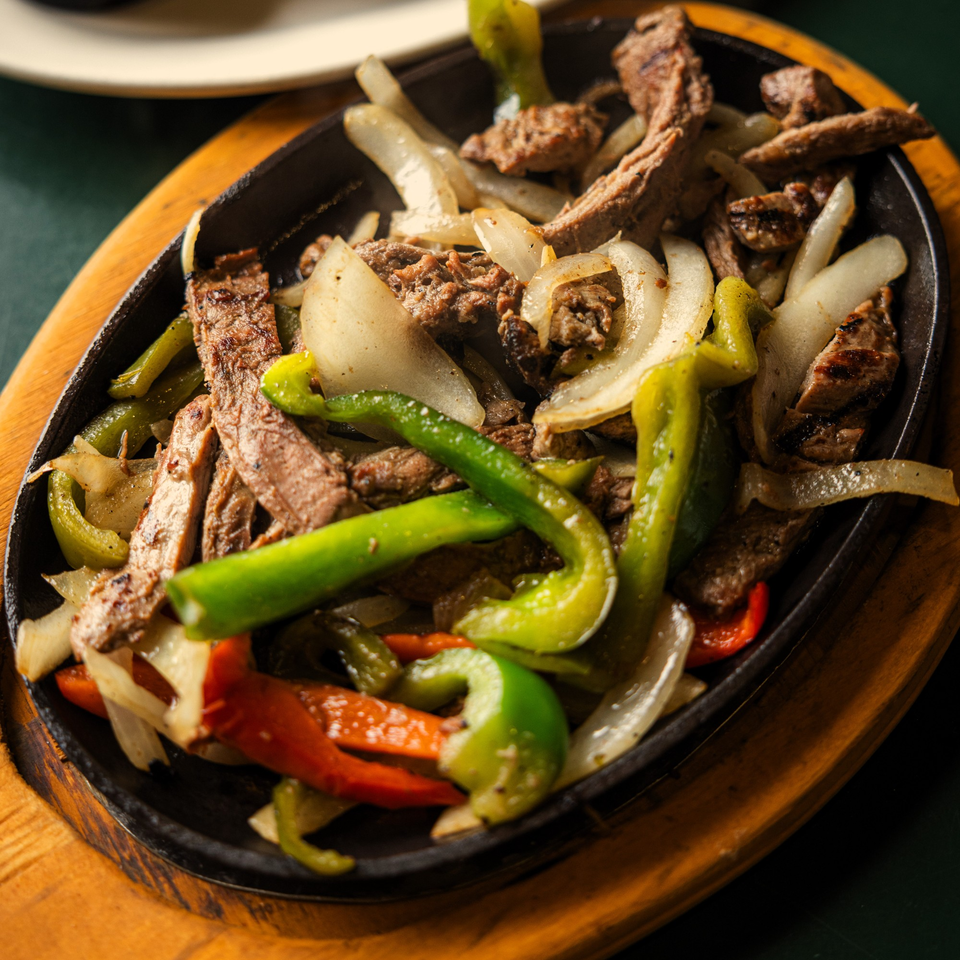 Sizzling La Casa del Sol fajitas with steak, green and red peppers, and onions in a cast iron skillet.